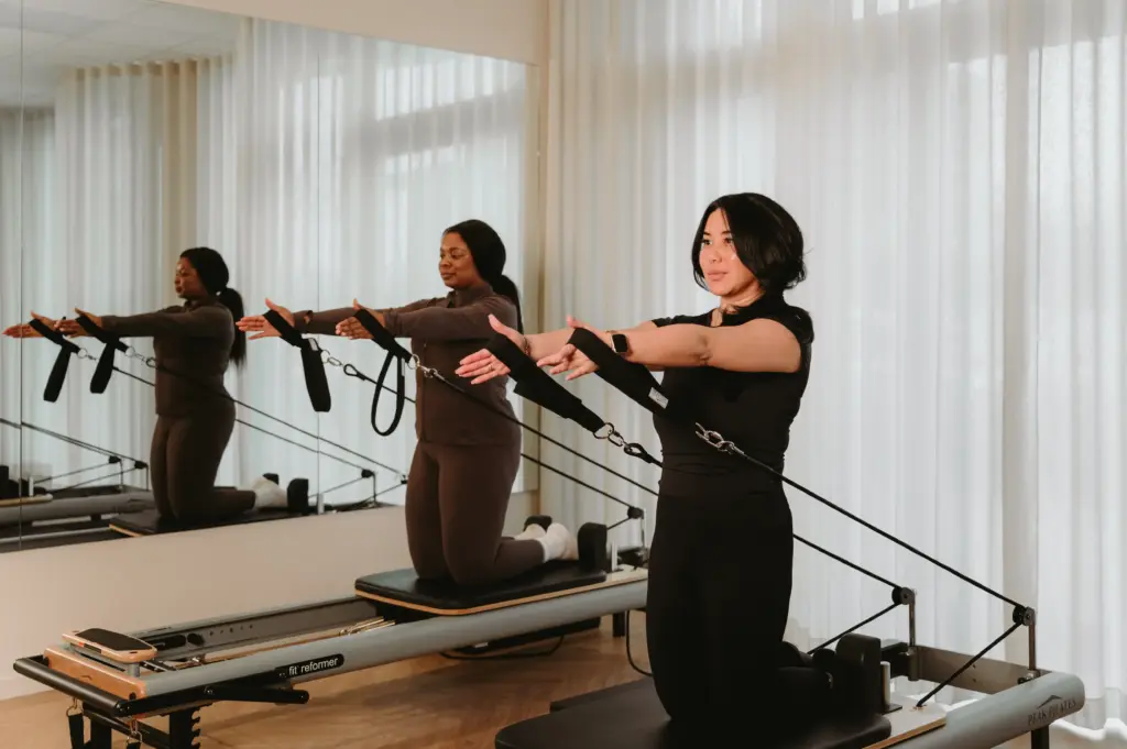 Women performing arm exercise on reformer Pilates machine in Zen Zest studio Goes with mirror view